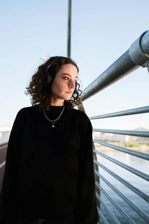 a woman standing on a bridge looking off into the distance, wearing a black sweater, curls, asher duran, high light on the left