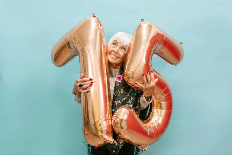 a woman holding two large balloons in front of a blue wall, pexels contest winner, 70 years old, golden number, 15081959 21121991 01012000 4k, inflatable