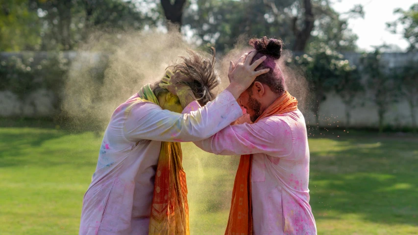 a couple of men standing on top of a lush green field, a colorized photo, pexels contest winner, holi festival of rich color, hair covering eyes, touching heads, college