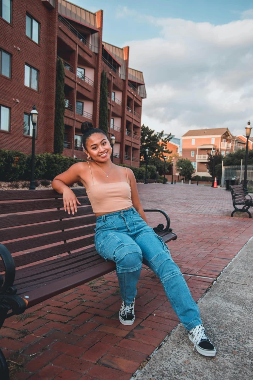 a woman sitting on top of a wooden bench, wearing a crop top, in a city square, cindy avelino, light skin tone