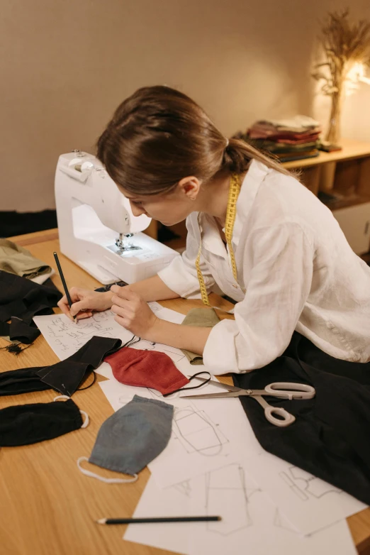 a woman sitting at a table in front of a sewing machine, masks, clothing design, carefully crafted, flat lay