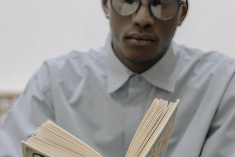 a man wearing glasses is reading a book, an album cover, by Carey Morris, pexels contest winner, hyperrealism, jemal shabazz, gif, holding a book, zoomed in