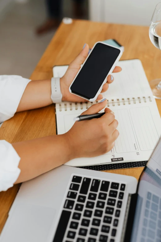 a woman sitting at a table with two laptops and a cell phone, trending on pexels, wearing a white button up shirt, diary on her hand, corporate phone app icon, scientific