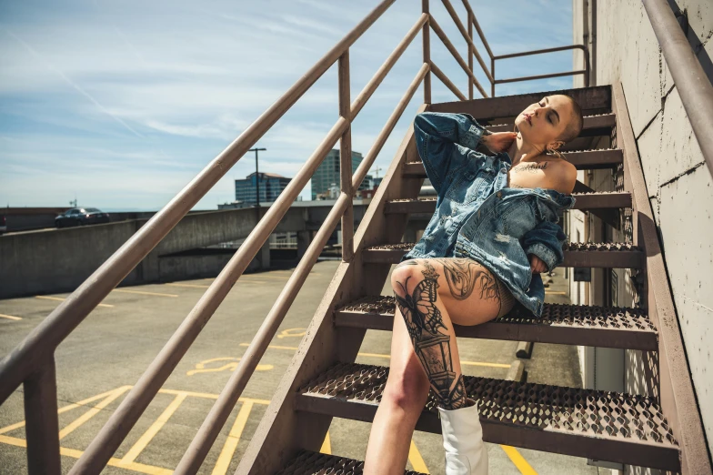 a woman sitting on a set of stairs, a tattoo, inspired by Elsa Bleda, pexels contest winner, graffiti, exposed thighs, on rooftop, non binary model, denim