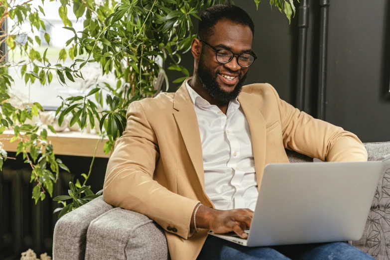 a man sitting on a couch using a laptop, pexels contest winner, brown skin man with a giant grin, wearing a suit and glasses, it specialist, thumbnail