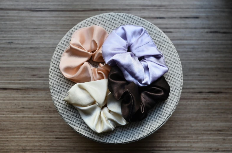 a white plate topped with three scrunches on top of a wooden table, by Nina Hamnett, instagram, silk colors, lilac, tan, hair bow