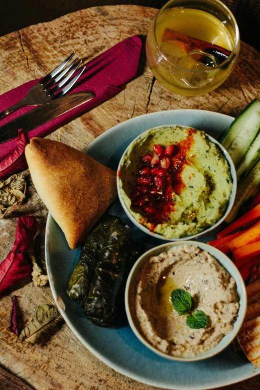 a plate of food sitting on top of a wooden table, middle eastern details, green and red tones, humus, ballard