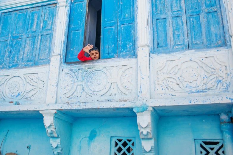 a person that is looking out of a window, inspired by Steve McCurry, pexels contest winner, arabesque, bright blue, waving at the camera, colorful house, khedival opera house