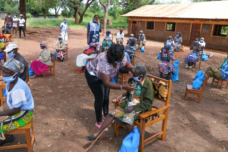 a group of people sitting around each other, by Ingrida Kadaka, process art, on a village, healthcare worker, covid, opening shot