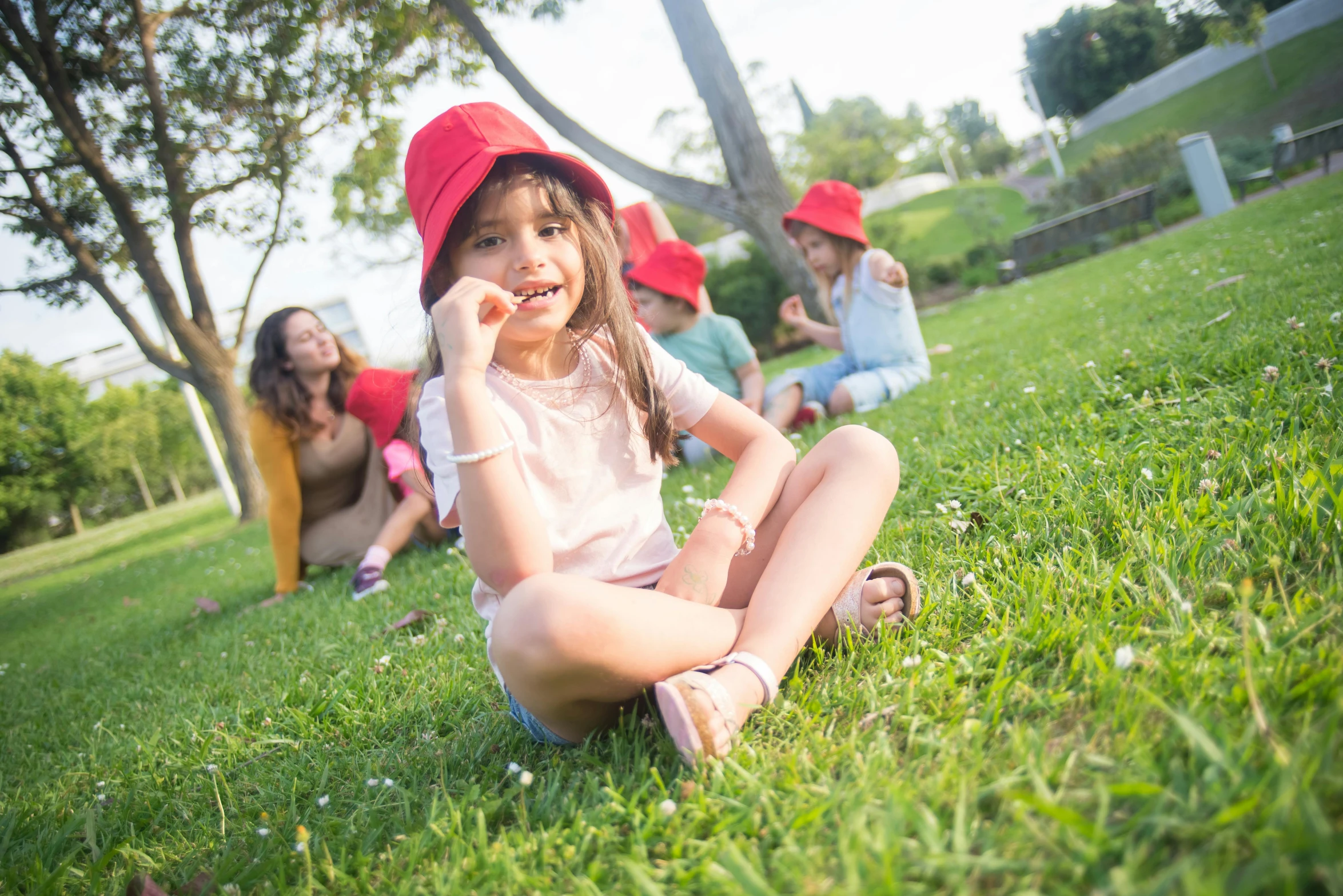 a group of children sitting on top of a lush green field, he has a red hat, at the park, she is wearing a hat, profile image