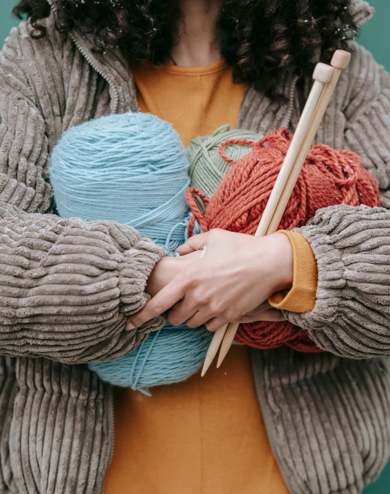 a woman holding a ball of yarn and knitting needles, by Jessie Algie, trending on pexels, ocher and turquoise colors, made of fabric, hugging, red and blue garments