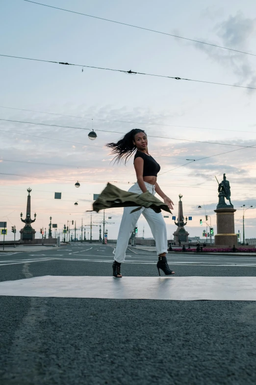 a woman walking across a street next to a statue, an album cover, pexels contest winner, happening, males and females breakdancing, in russia, sun set, beautiful city black woman only