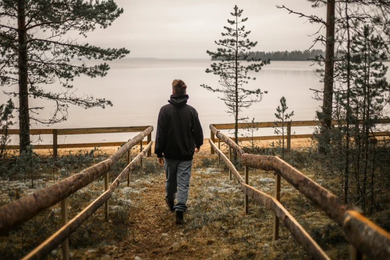 a man walking down a path towards a body of water, by Grytė Pintukaitė, unsplash, northern finland, standing in an arena, camp, looking out at the ocean