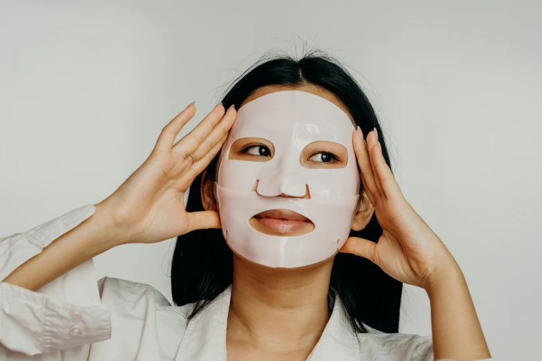 a woman putting a mask on her face, an album cover, trending on pexels, mingei, silicone skin, symmetrical face happy, asian female, wearing translucent sheet