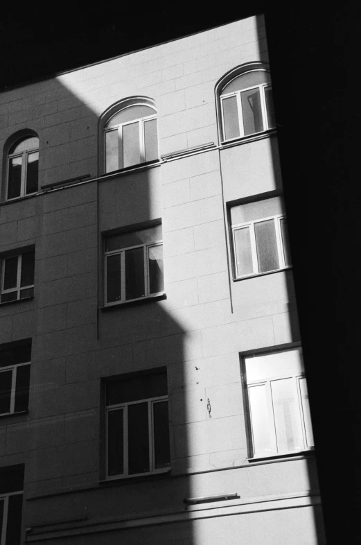 a black and white photo of a tall building, a black and white photo, inspired by André Kertész, unsplash, light and space, the sun reflecting on a window, in moscow centre, shady alleys, ambient occlusion:3