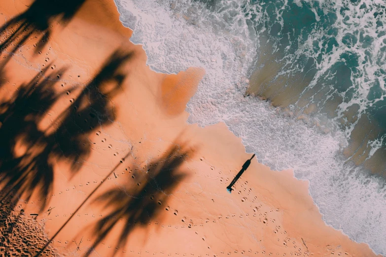 a person walking on a beach next to the ocean, pexels contest winner, bird\'s eye view, tropical palms, orange hue, lying down