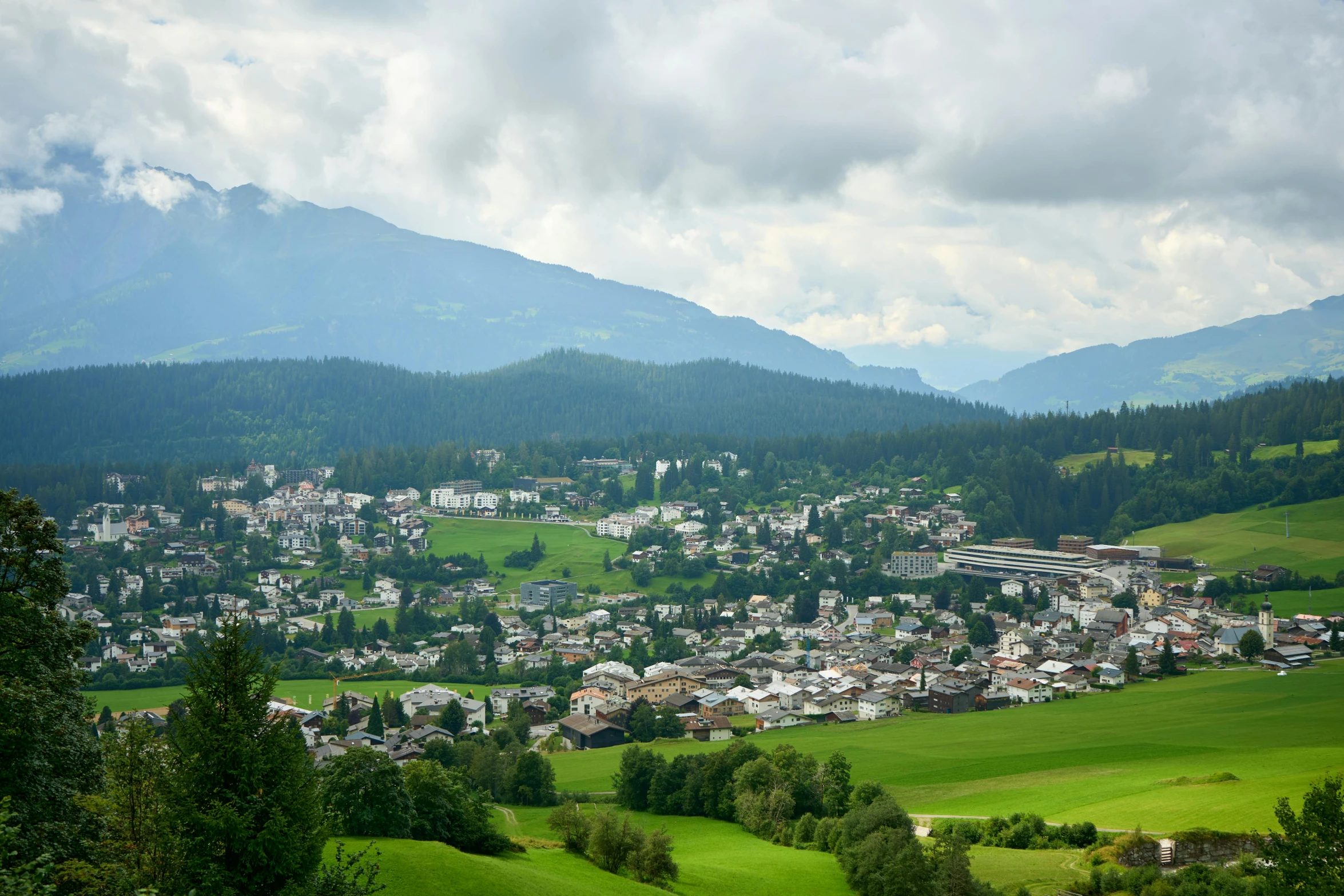 a view of a town with mountains in the background, by Ulrich Leman, pexels contest winner, a green, lush surroundings, avatar image, wide high angle view