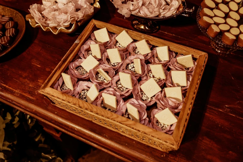 a table topped with lots of desserts on top of a wooden table, a picture, by Alice Mason, pexels, art nouveau, many origami roses, gold and purple, cigarrette boxes at the table, square