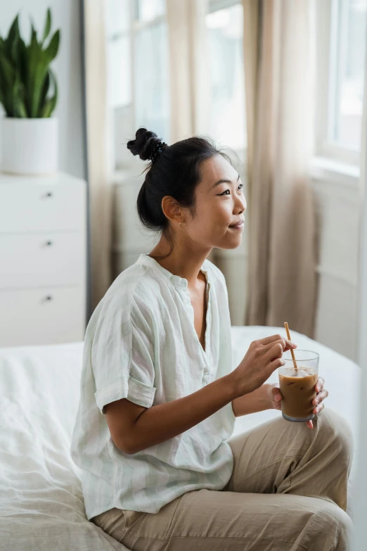 a woman sitting on a bed holding a cup of coffee, inspired by Ruth Jên, trending on pexels, happening, drinking boba tea, drinking cough syrup, asian male, profile image