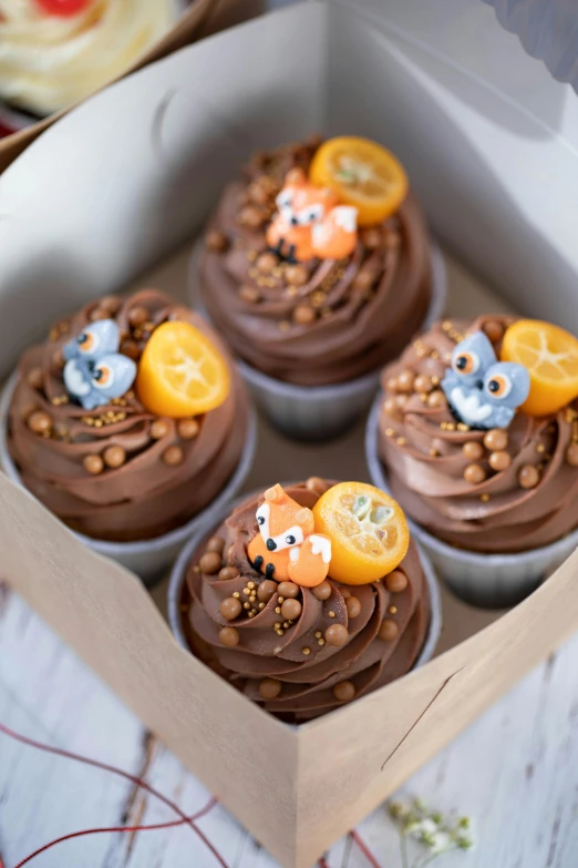 a box filled with cupcakes sitting on top of a table, by Basuki Abdullah, 3 woodland critters, dark grey and orange colours, thumbnail, dessert