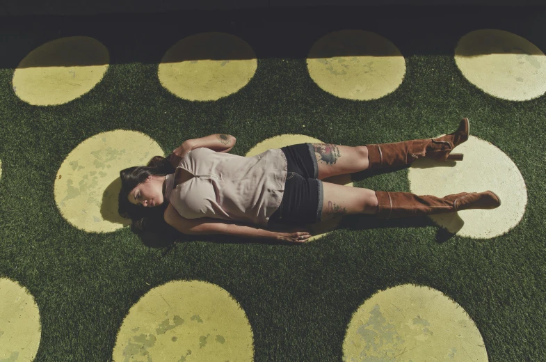 a woman laying on top of a grass covered field, pexels contest winner, land art, yellow carpeted, circles, retro vibe, on an empty stage from above