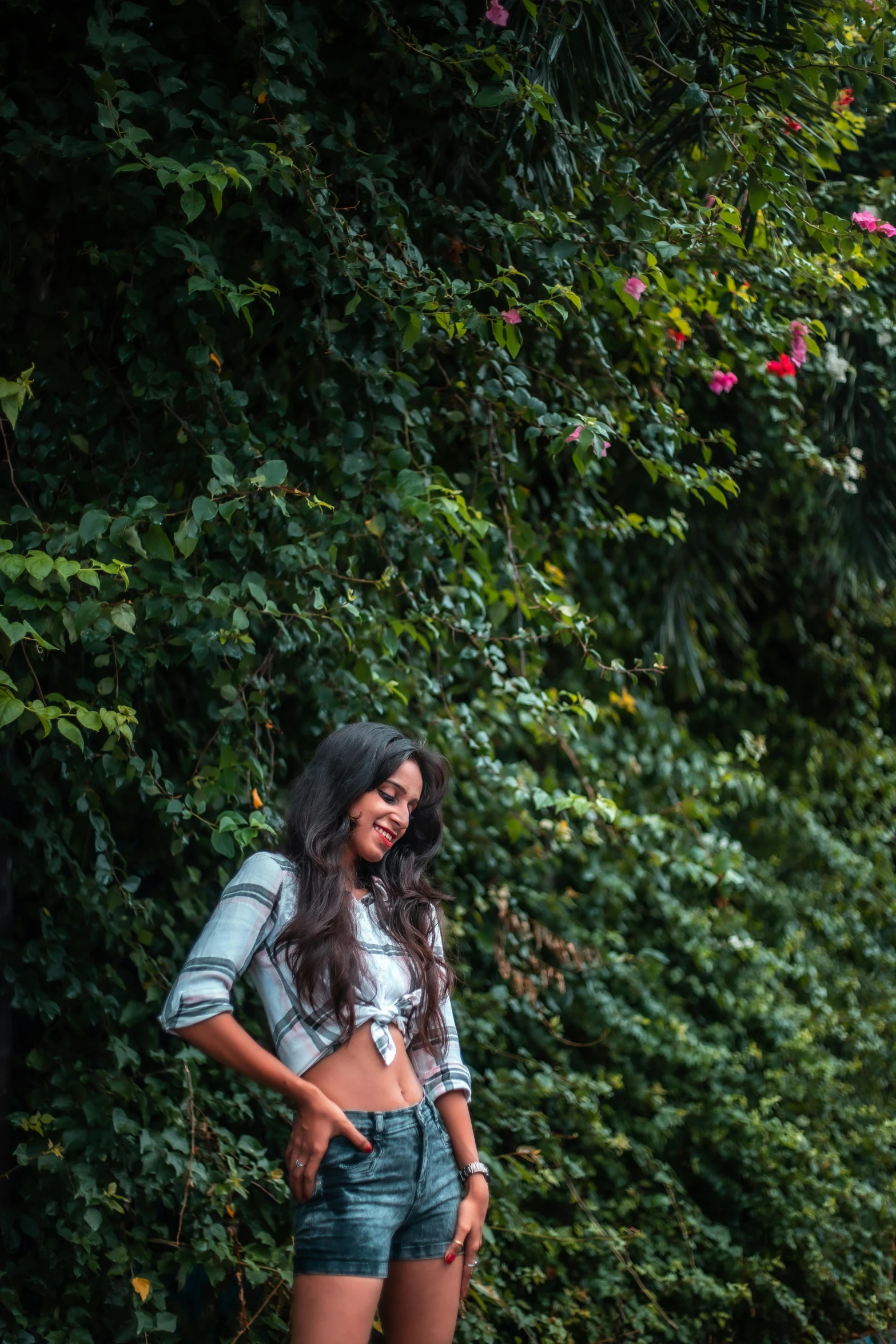 a woman standing in the middle of a road, lush greenery, wearing crop top, vines on the walls, smiling