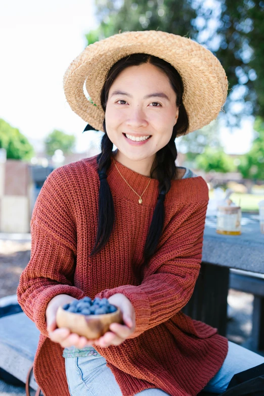 a woman sitting on a bench holding a donut, inspired by Ruth Jên, pexels contest winner, wearing a blue berries, portrait of mulan, wearing casual sweater, wearing straw hat