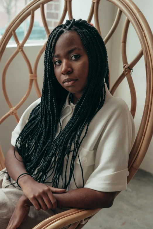 a woman sitting in a wicker chair in front of a window, by Lily Delissa Joseph, pexels contest winner, black arts movement, long black braided hair, kara walker james jean, teenage girl, promo image