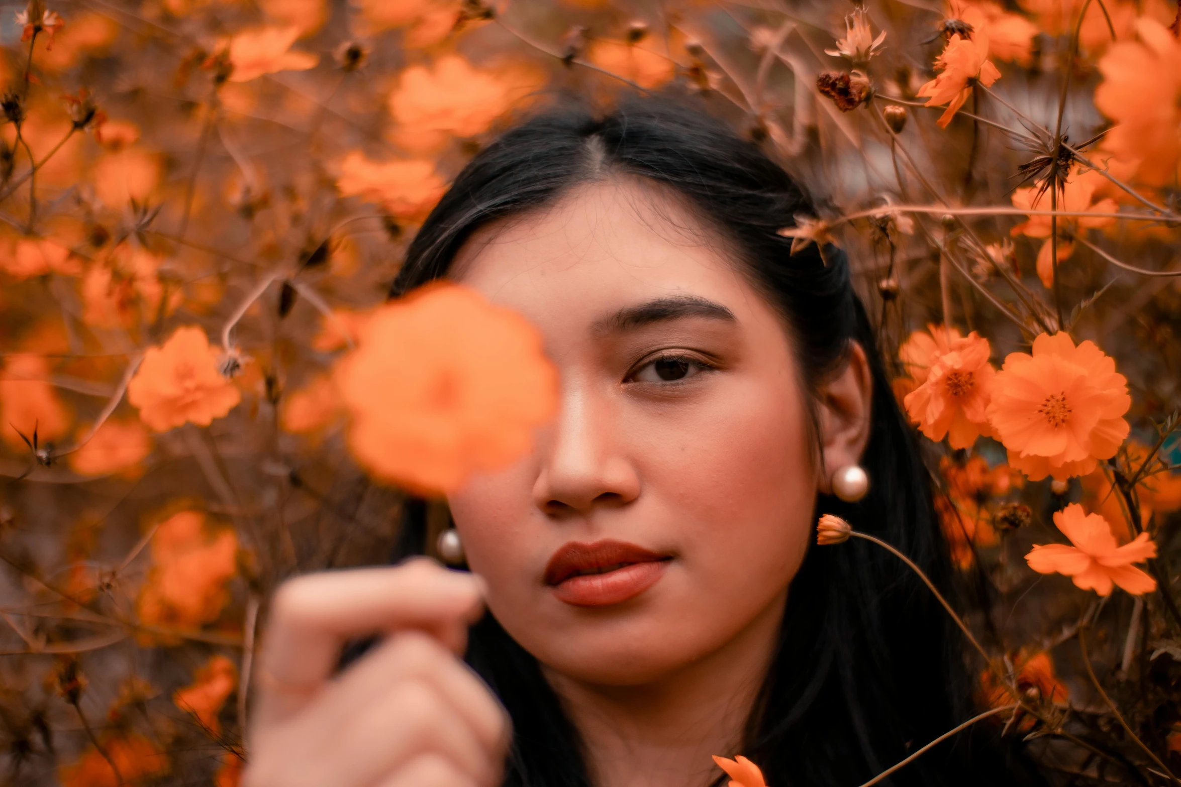 a woman holding a flower in front of her face, pexels contest winner, orange color theme, avatar image, asian face, fall season