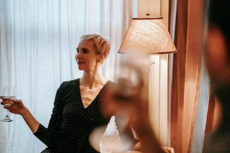 a woman sitting in a chair holding a glass of wine, by Carey Morris, pexels contest winner, standing near a window, girl with short white hair, hotel room, jovana rikalo