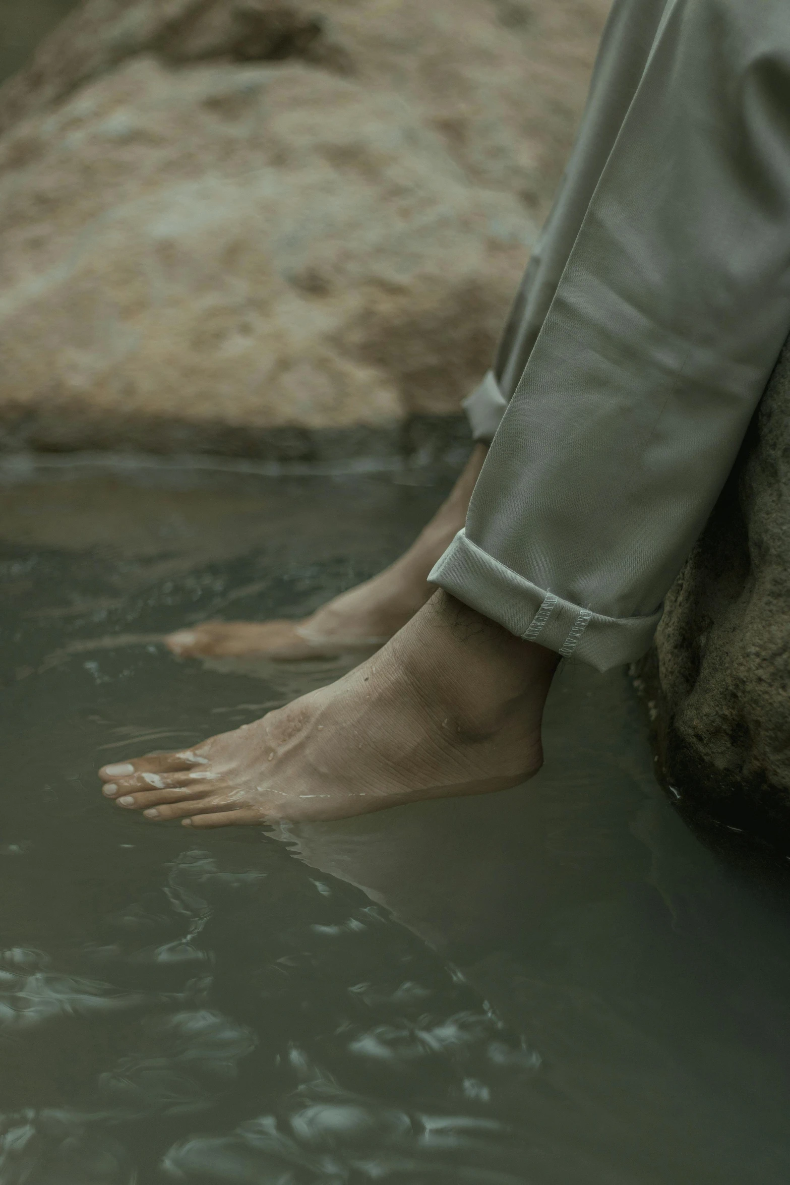 a person sitting on a rock in a body of water, by Elsa Bleda, renaissance, detailed foot shot, [ cinematic, alessio albi, grey