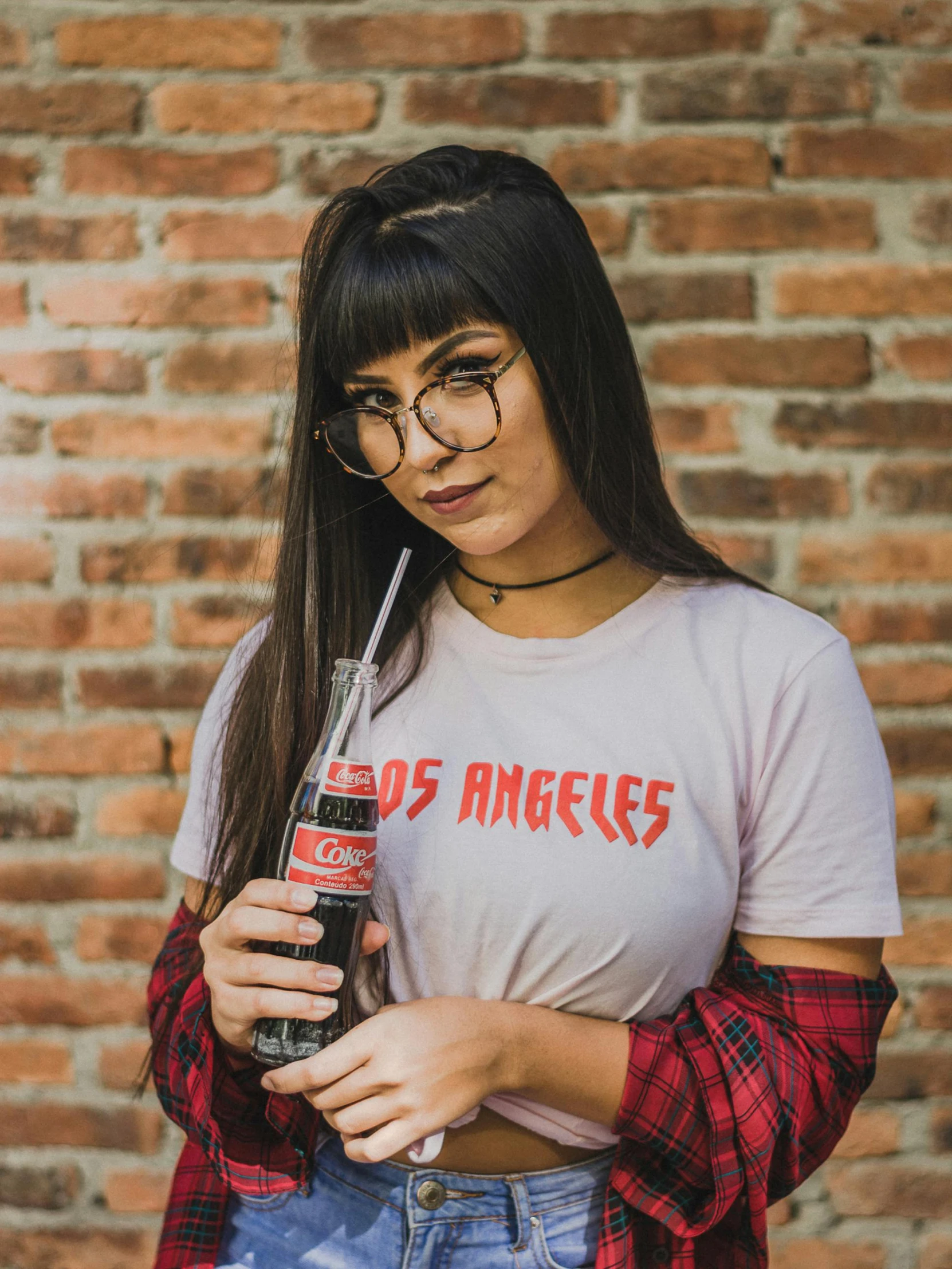 a woman standing in front of a brick wall holding a coke, pexels contest winner, los angelos, wearing a t-shirt, nerds, profile image