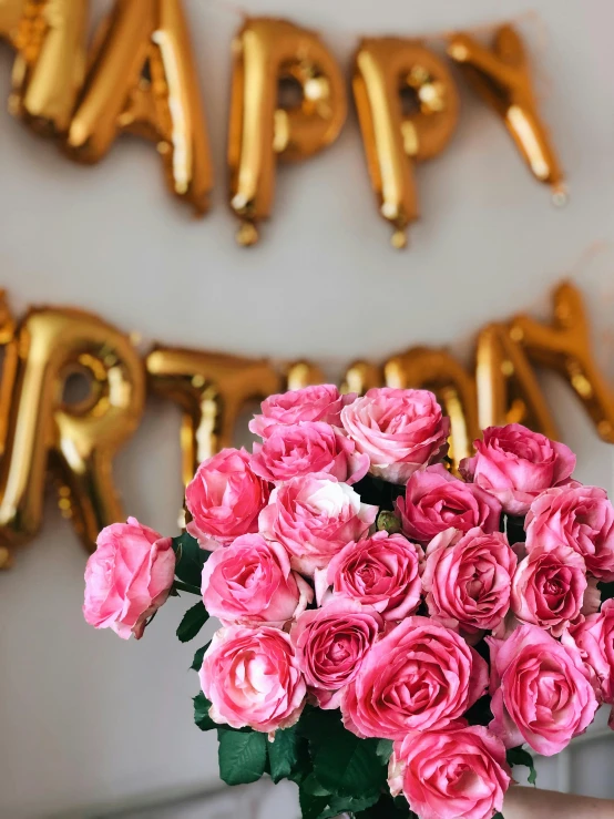 a person holding a bouquet of pink roses, by Robbie Trevino, happening, party balloons, banner, close - up photograph, gold