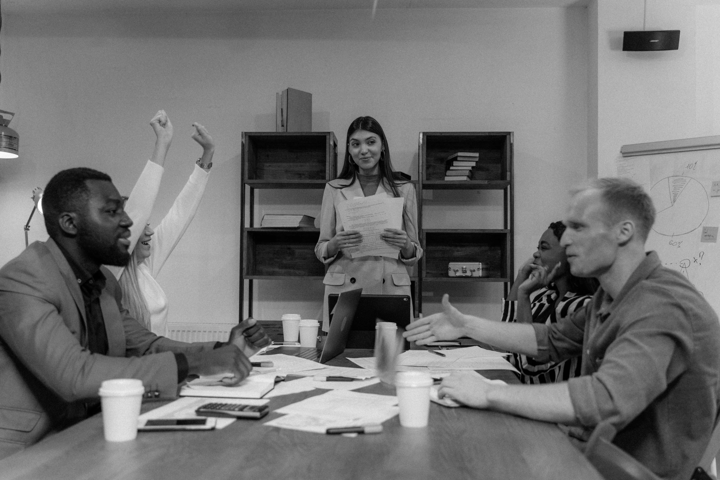 a group of people sitting around a wooden table, a black and white photo, pexels contest winner, giving a speech, sat in an office, hands in the air, mahira khan as a d&d wizard