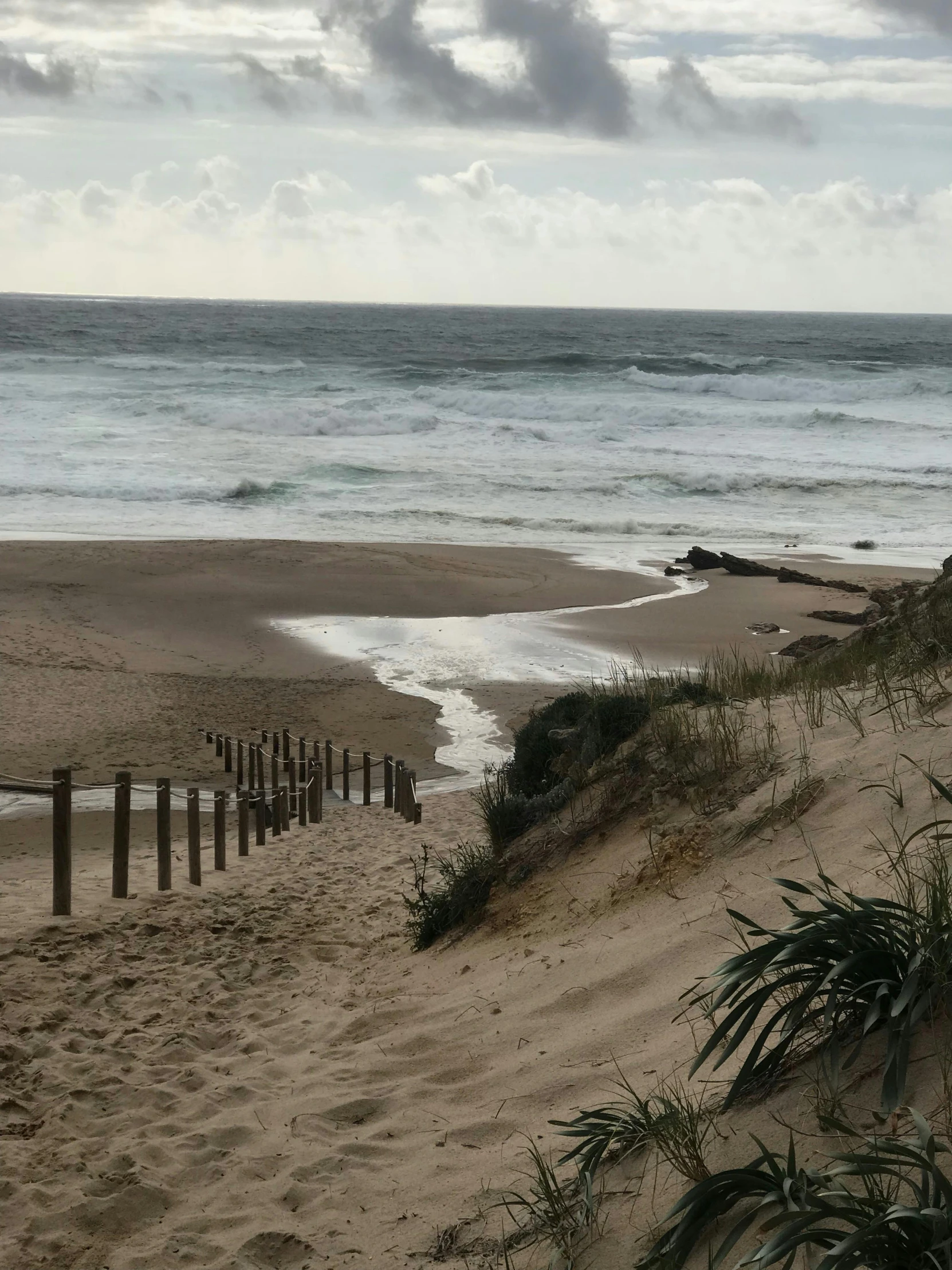 a man standing on top of a sandy beach next to the ocean, by Elizabeth Durack, happening, looking around a corner, trending photo, no filter, slight overcast