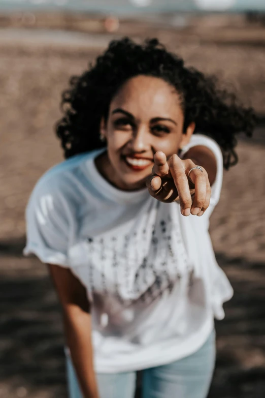 a woman standing on top of a sandy beach, she has perfect white teeths, hand gesture, woman in streetwear, portrait featured on unsplash