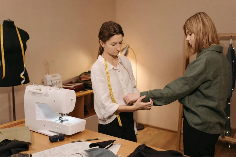 two women standing in front of a sewing machine, by Emma Andijewska, trending on pexels, renaissance, measurements, from the elbow, low quality photo, thumbnail