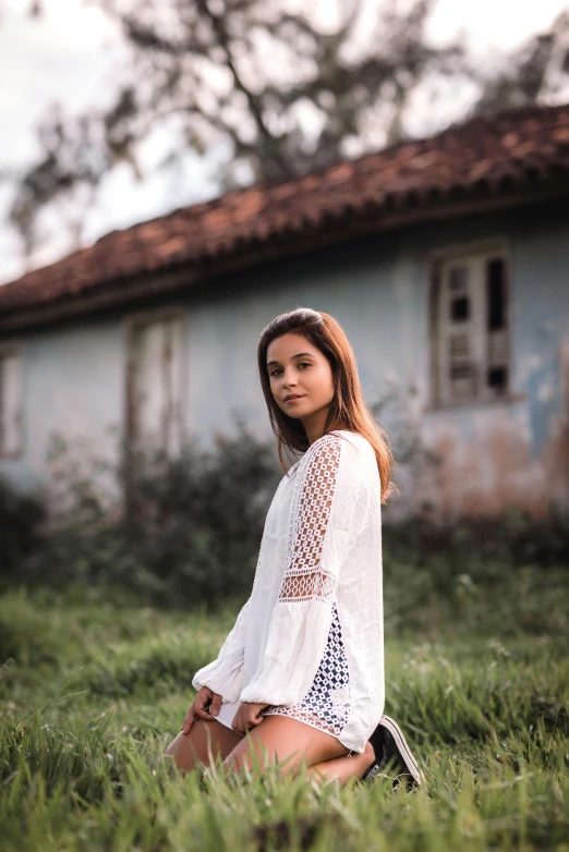 a woman sitting in the grass in front of a house, inspired by Elsa Bleda, pexels contest winner, white clothing, portrait image, girl standing, tourist photo