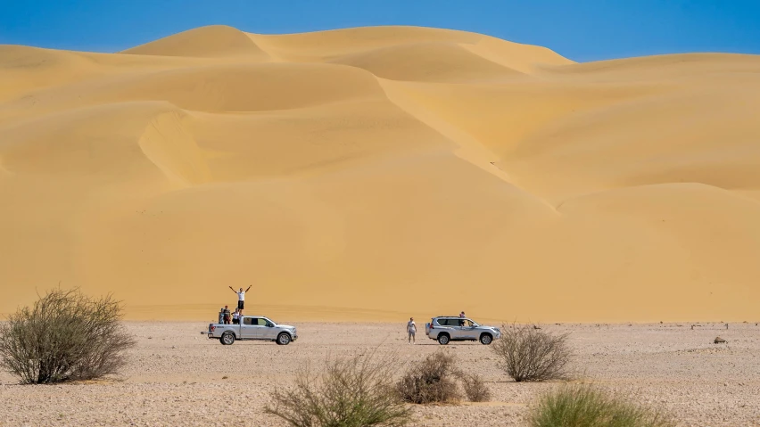 a couple of cars that are in the sand, a picture, les nabis, majestic dunes, onlookers, exterior shot, an intricate