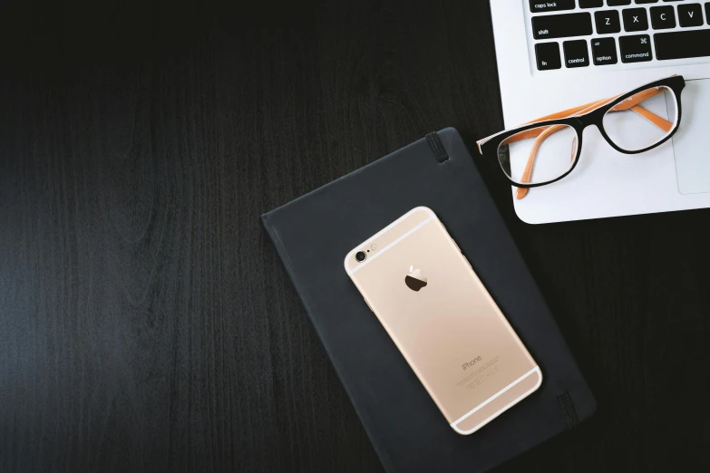 an iphone sitting on top of a table next to a laptop, by Niko Henrichon, trending on unsplash, black and gold, square, spectacled, medium-shot