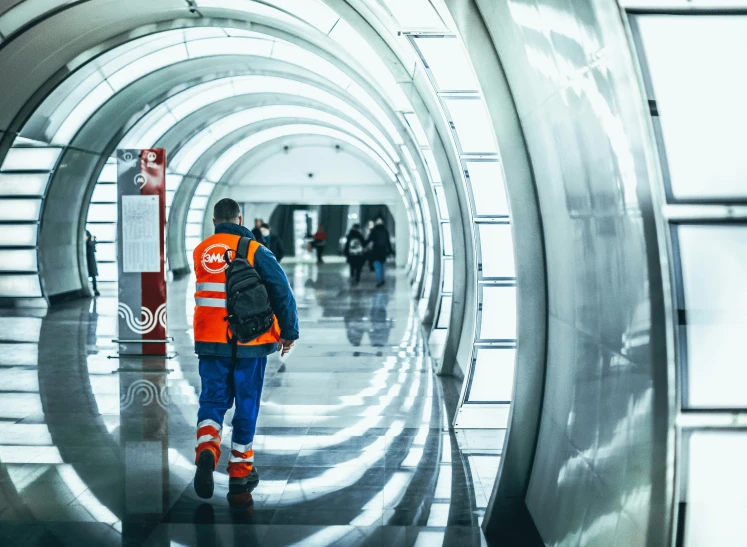 a man in an orange vest walking through a tunnel, by Adam Marczyński, pexels contest winner, arbeitsrat für kunst, subway station, working clothes, shiny reflective surfaces, a photo of a man