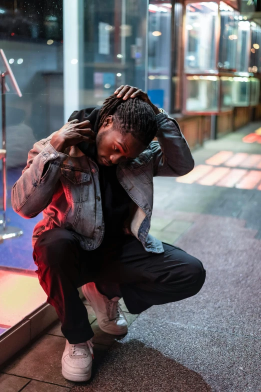 a man squatting on the ground in front of a store, an album cover, trending on pexels, happening, dreads, depressed dramatic bicep pose, nightlife, black teenage boy