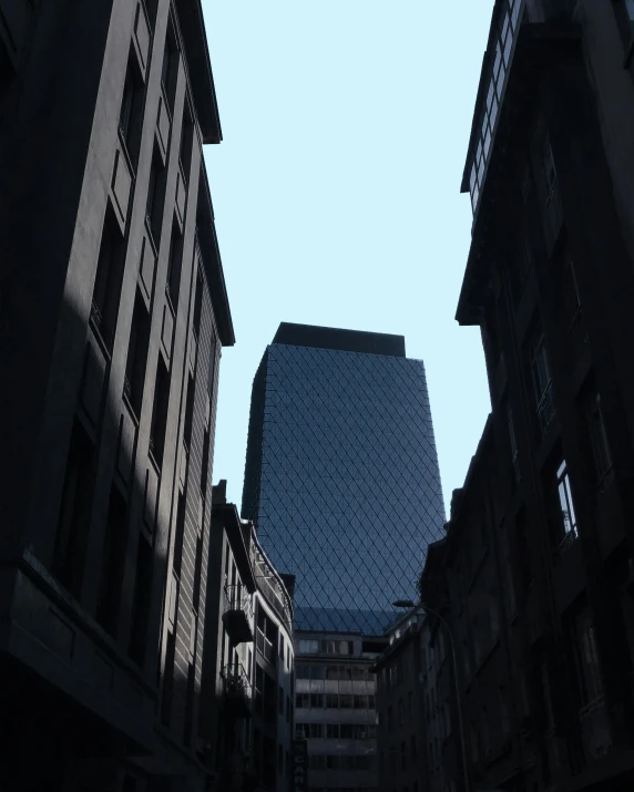 a tall building towering over a city street, by IAN SPRIGGS, barely visible from the shadows, in london, low quality photo