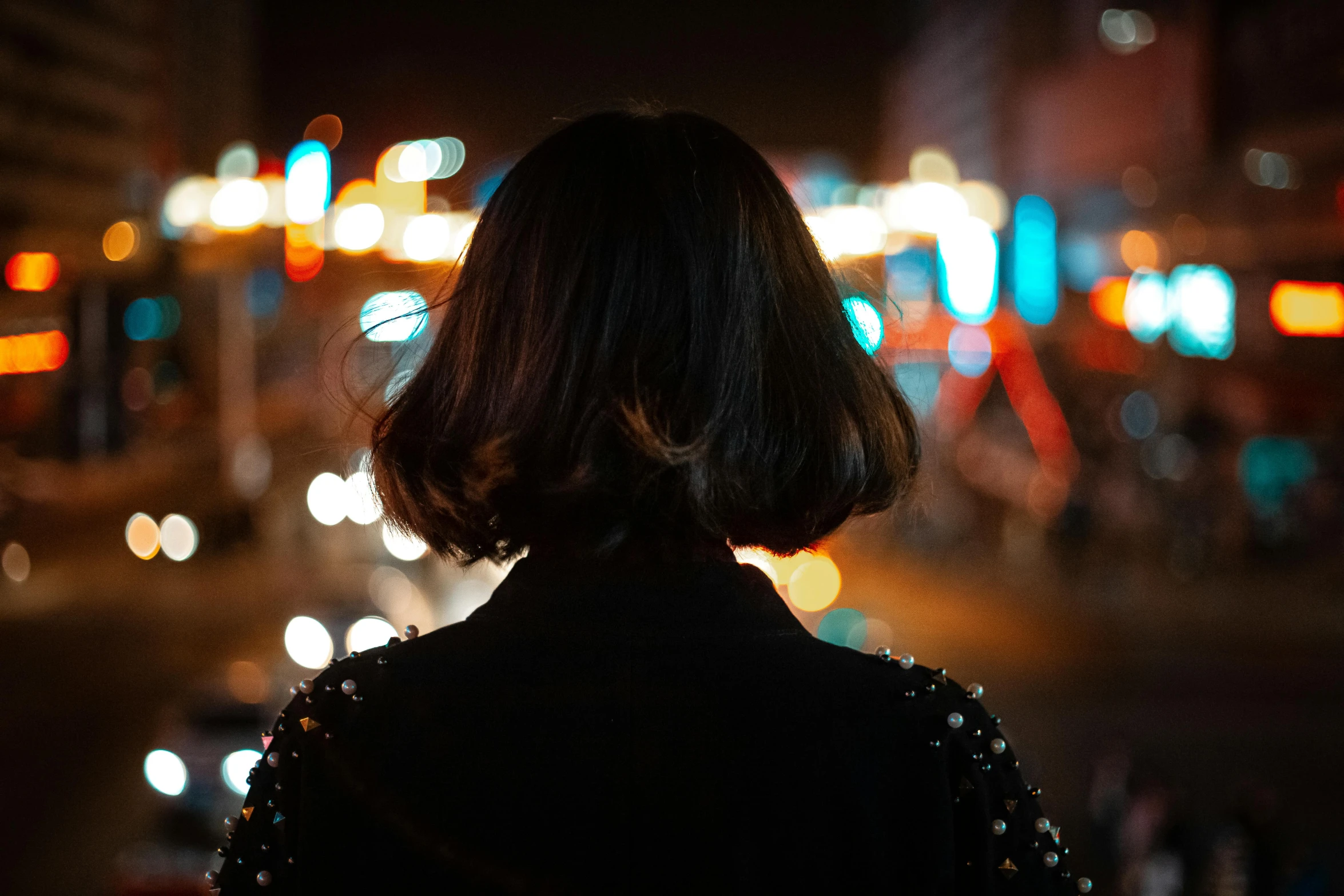 a woman standing on a city street at night, pexels contest winner, happening, black bob hair, back of head, bokeh. debadged, with a bob cut
