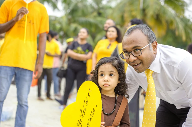 a man standing next to a little girl holding a sign, inspired by Ismail Gulgee, pexels contest winner, hurufiyya, yellow hue, sri lanka, inauguration, profile pic