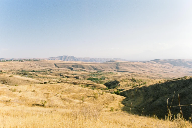 a man standing on top of a grass covered hillside, by Edward Avedisian, unsplash, les nabis, mesopotamic, panorama distant view, slightly tanned, with rolling hills