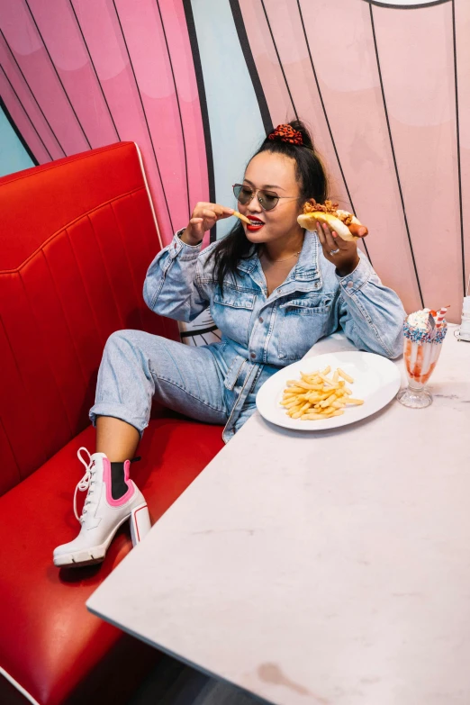 a woman sitting at a table with a plate of food, inspired by Pia Fries, trending on pexels, pop art, pink shoes, wearing double denim, vanessa morgan, hot dog