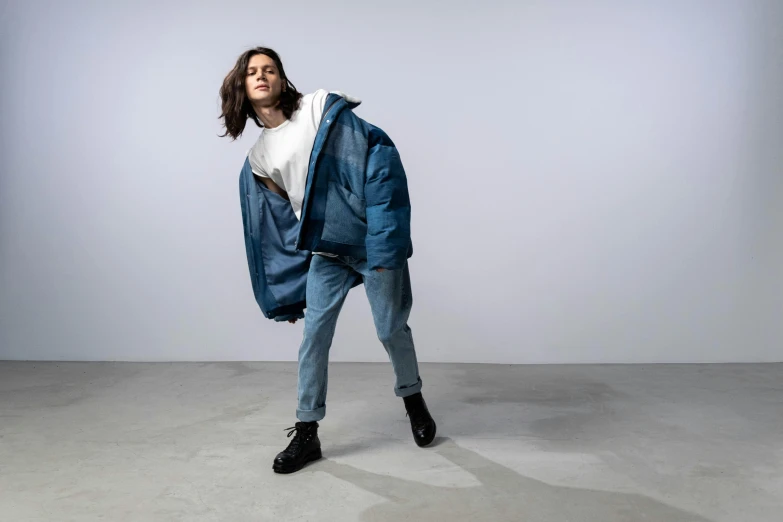 a man with long hair wearing a blue jacket and jeans, an album cover, trending on unsplash, hyperrealism, full body sarcastic pose, model wears a puffer jacket, portrait androgynous girl, in a fighting pose