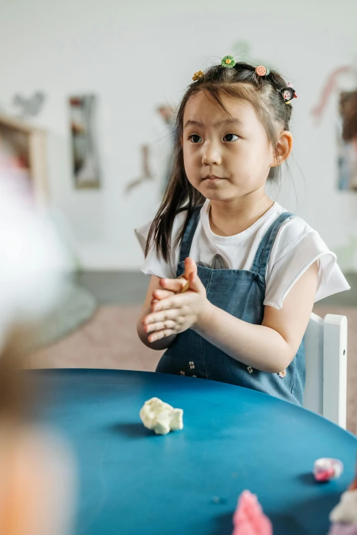 a little girl that is sitting at a table, partially cupping her hands, butter sculpture, annoyed, in a classroom