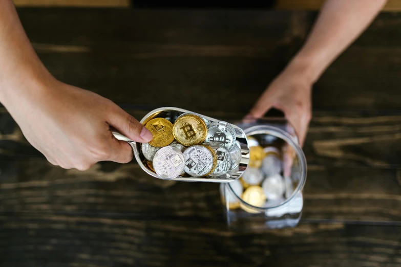 a person holding a container filled with coins, by Adam Marczyński, trending on unsplash, renaissance, edible crypto, back of hand on the table, “ iron bark, press shot